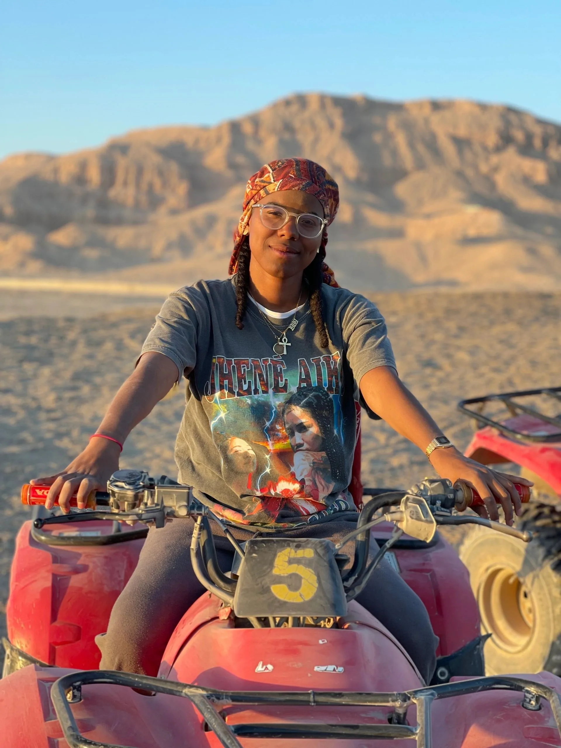 A person seated on a red quad bike with mountains behind them.