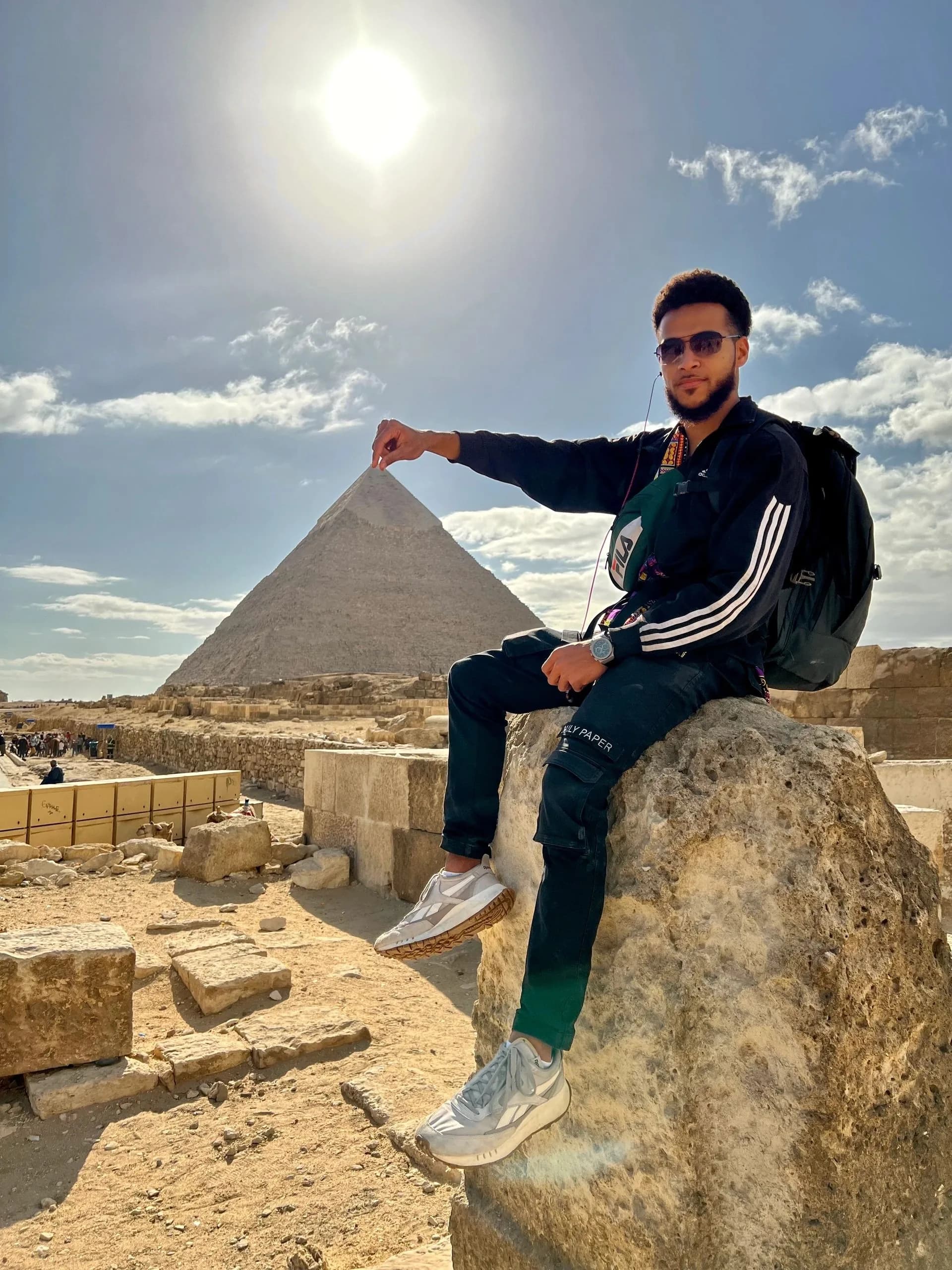 A person seated on a rock with a pyramid behind them.