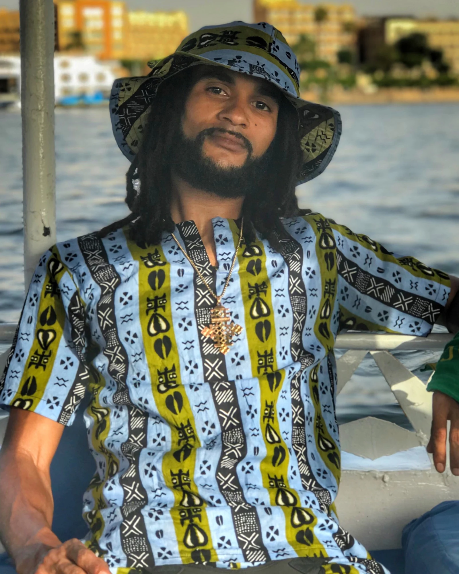 Omega Axsal, seated by the water in a patterned shirt and matching hat.