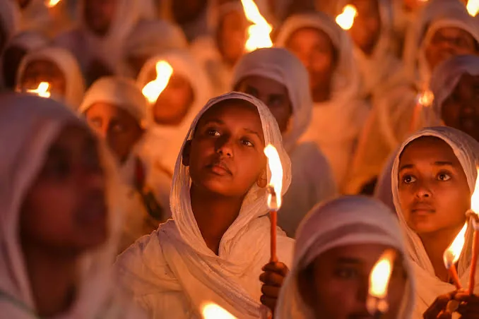 Faces lit by candlelight among a crowd in white
